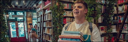 Bannière Heartstopper - Isaac achète une pile de livres dans une librairie parisienne